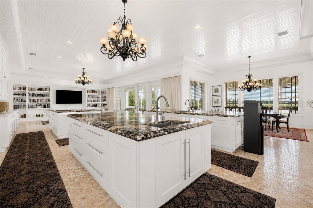 A spacious white kitchen features two large islands with dark stone countertops and chandeliers — 9508 WINDY RIDGE ROAD, WINDERMERE, FL