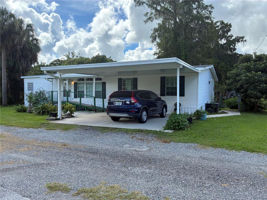 A white single-story manufactured home features a carport, a wheelchair ramp, and a gravel driveway — 457 NW 5TH ROAD, LAKE PANASOFFKEE, FL