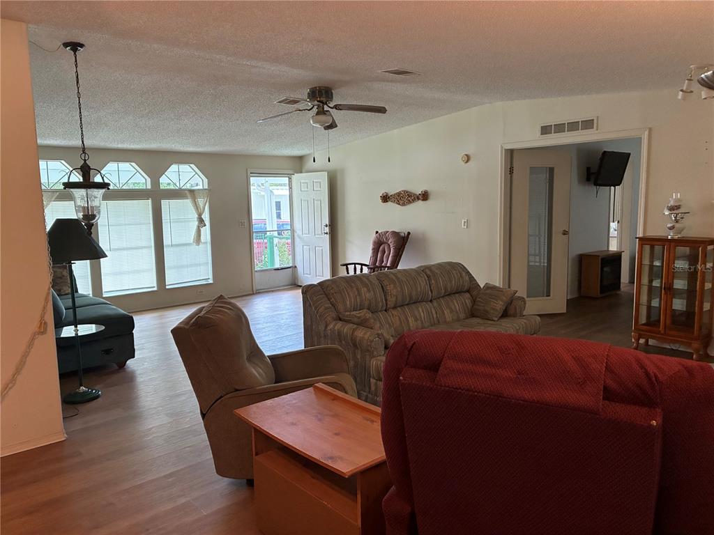 A living room features wood-look flooring, a ceiling fan, and a view toward an exterior door — 457 NW 5TH ROAD, LAKE PANASOFFKEE, FL