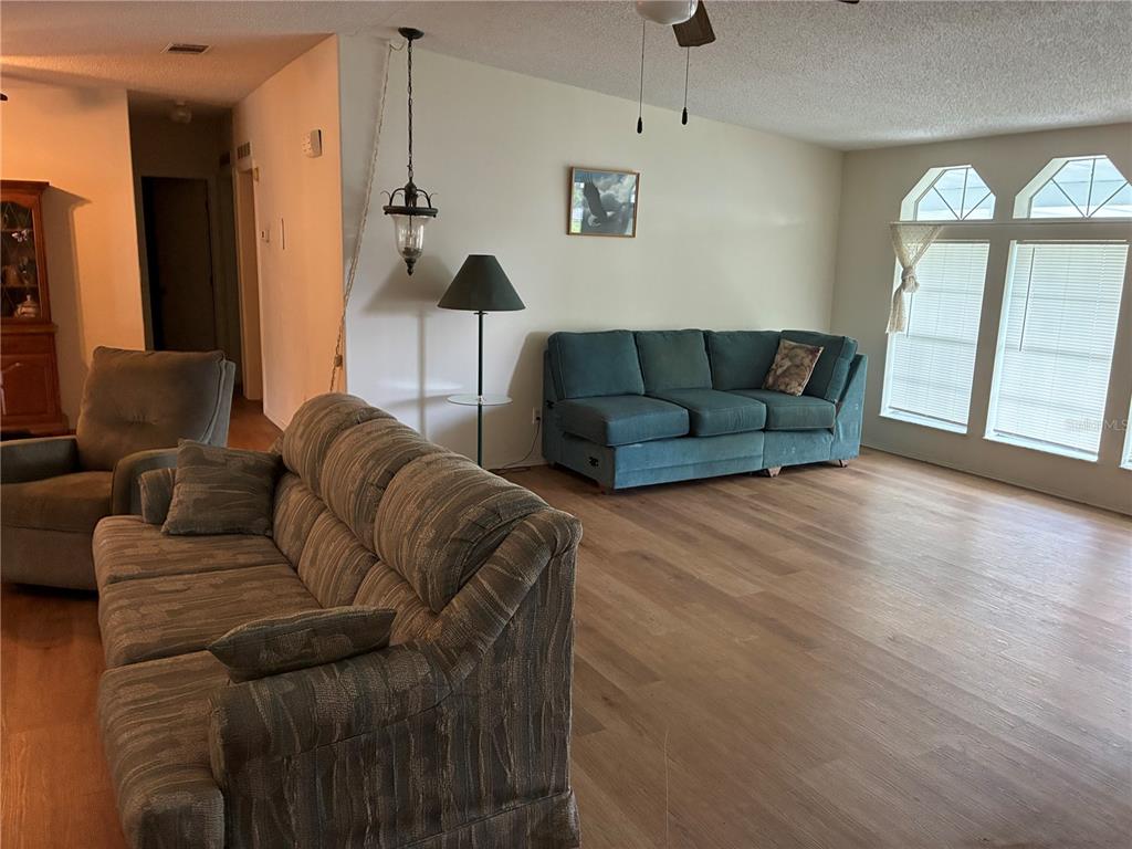 A living room features wood-look flooring, two sofas, a floor lamp, and large arched windows — 457 NW 5TH ROAD, LAKE PANASOFFKEE, FL