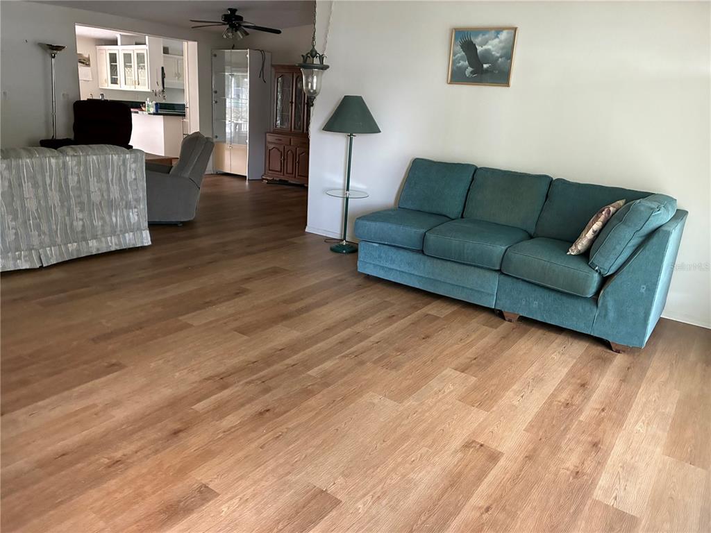A living room features light wood-look flooring, a teal sofa, and an adjacent dining area — 457 NW 5TH ROAD, LAKE PANASOFFKEE, FL