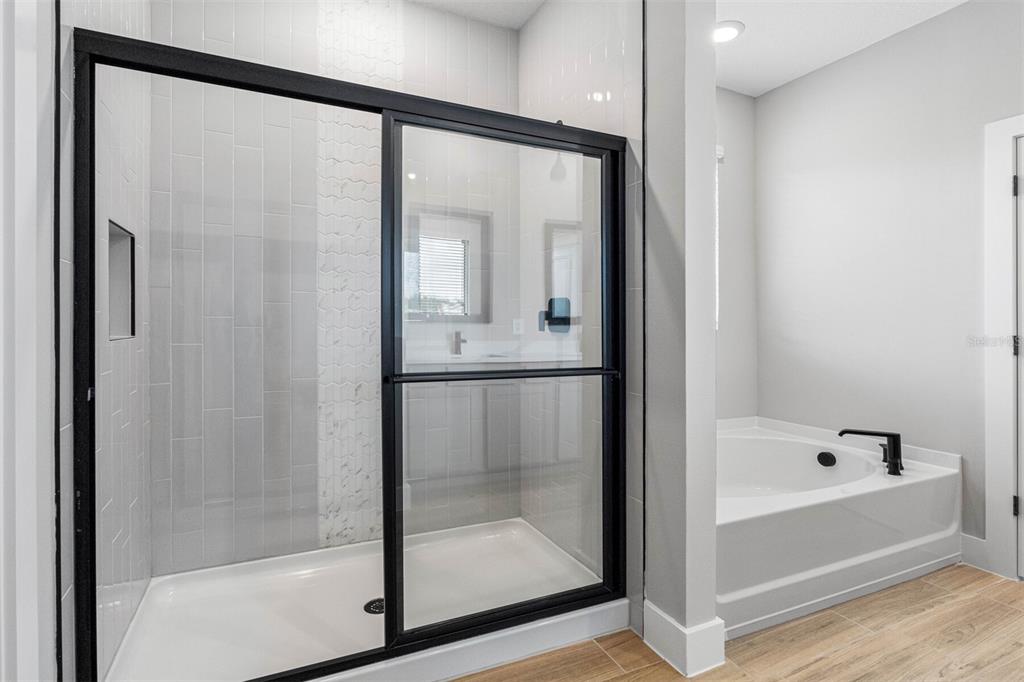 A bathroom features a glass-enclosed shower with black framing next to a white soaking tub — 13439 WALDEN SHEFFIELD ROAD, DOVER, FL