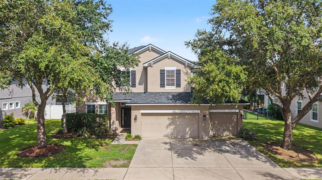 A two-story suburban house with a tan stucco exterior, a three-car garage, and mature trees — 2622 RED FERN DRIVE, DOVER, FL