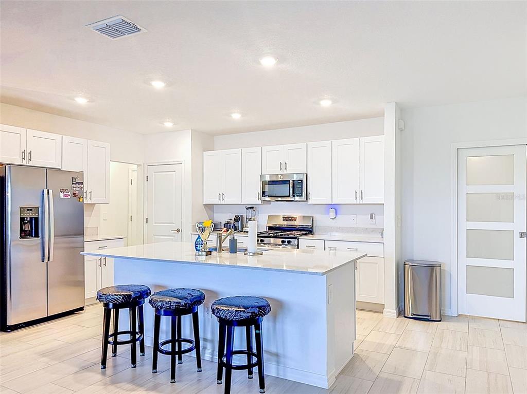 A modern kitchen features white cabinetry, a central island with bar stools, and stainless appliances — 12227 RADIANT GEM TRL, PARRISH, FL