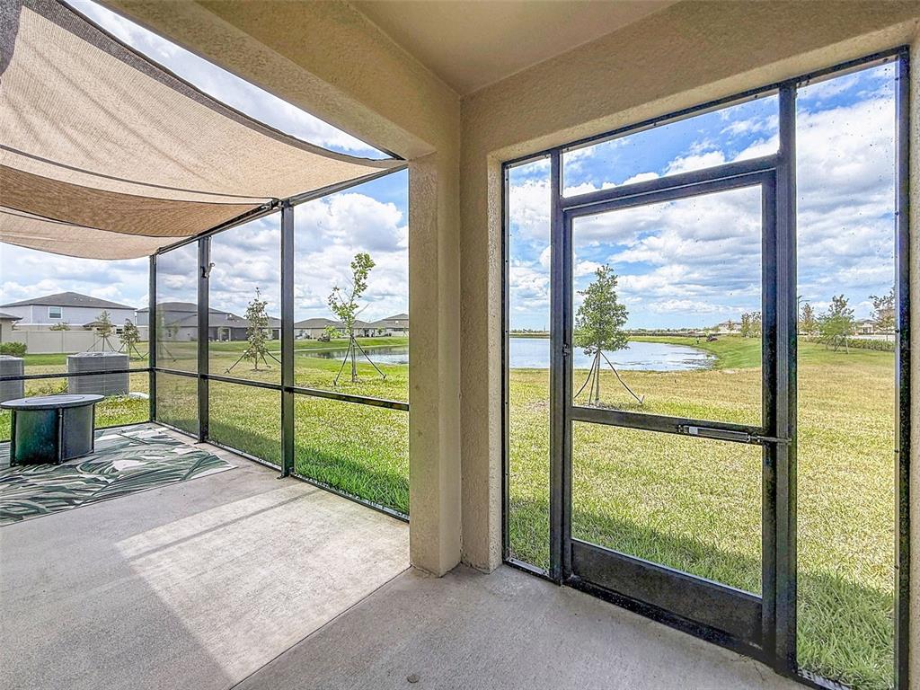 A screened-in patio features a concrete floor, a shade sail, and views of a pond — 12227 RADIANT GEM TRL, PARRISH, FL