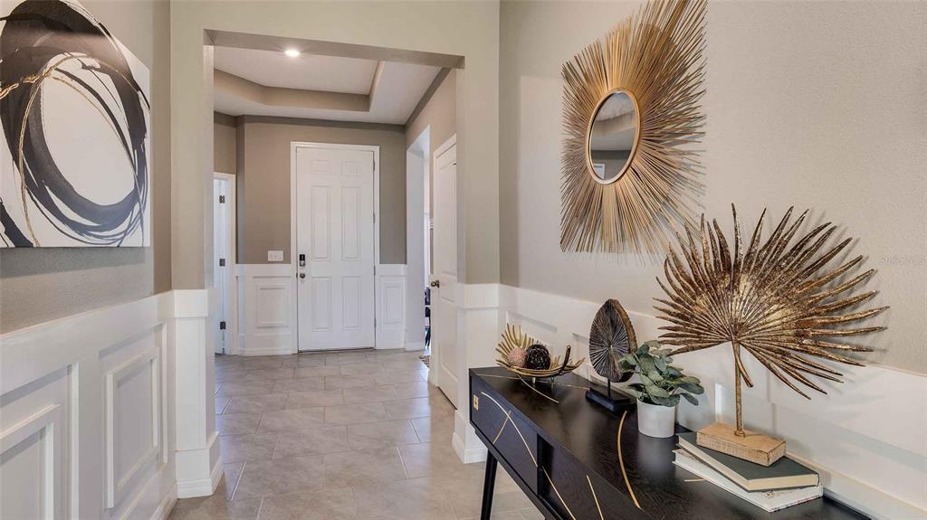 A foyer features white wainscoting, tile flooring, a black console table, and gold wall decor — 32693 DULUTH DRIVE, WESLEY CHAPEL, FL