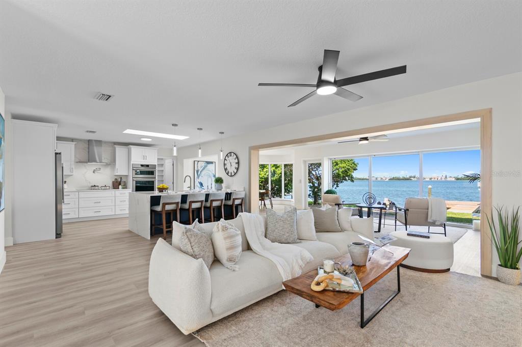 An open-concept living room and kitchen feature light wood floors, white cabinetry, and waterfront views — 202 DRIFTWOOD LANE, LARGO, FL