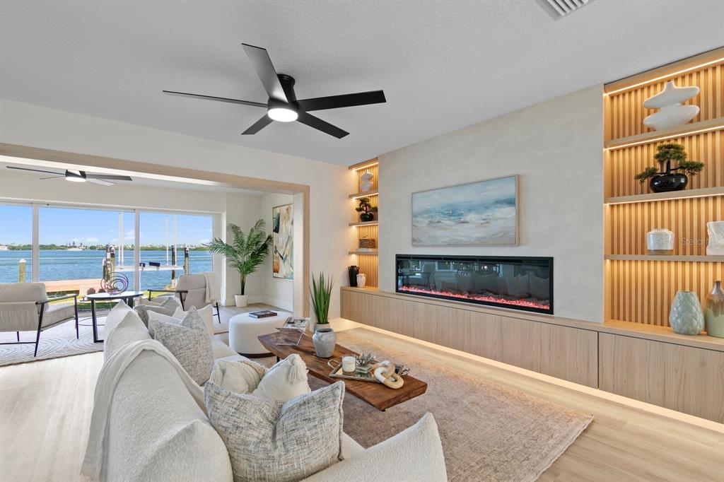 A modern living room features a linear fireplace, built-in shelving, and a view of water — 202 DRIFTWOOD LANE, LARGO, FL