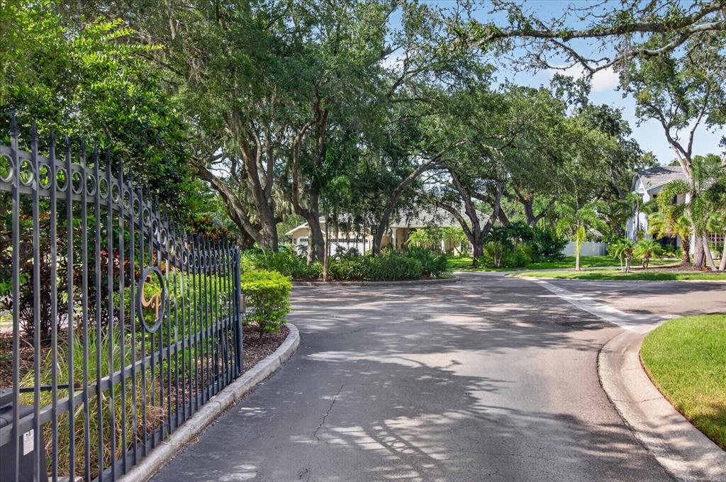 A black metal gate opens onto a paved driveway leading toward a house under trees — 8735 CRESCENT FOREST BOULEVARD, NEW PORT RICHEY, FL