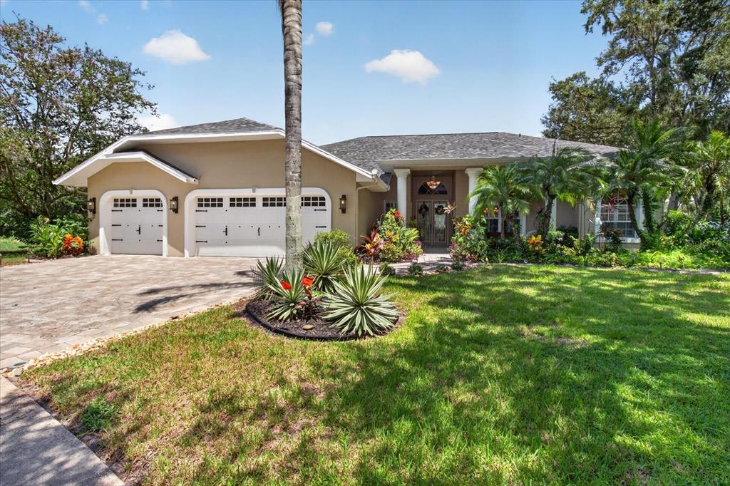 A single-story house with a two-car garage, a paved driveway, and lush tropical landscaping — 8735 CRESCENT FOREST BOULEVARD, NEW PORT RICHEY, FL