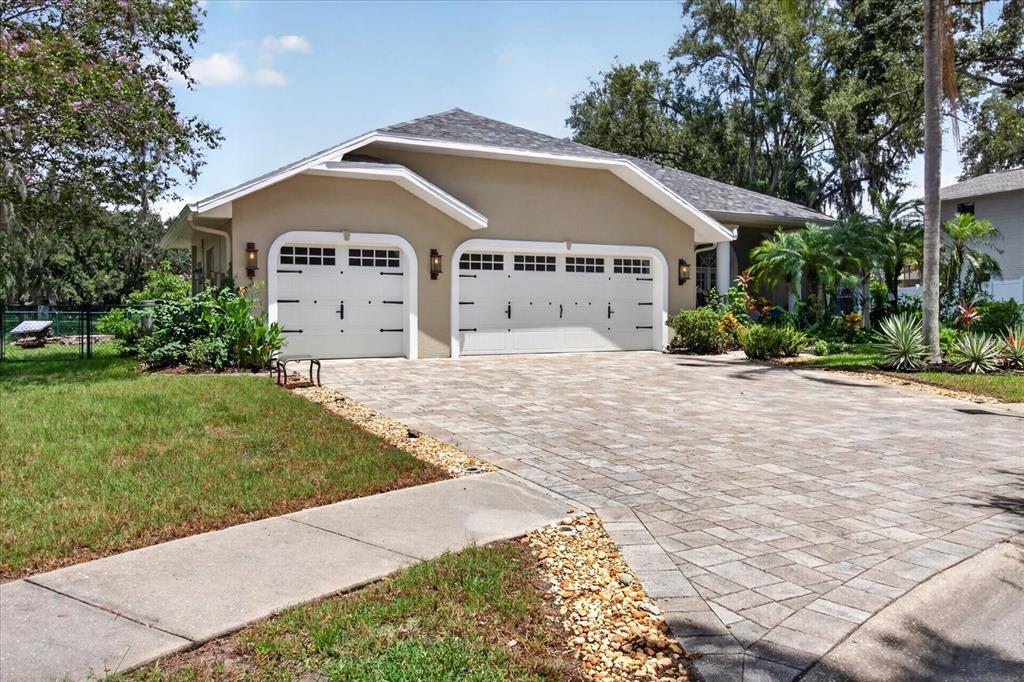 A beige house with a two-car garage and a paved driveway sits on a lawn — 8735 CRESCENT FOREST BOULEVARD, NEW PORT RICHEY, FL