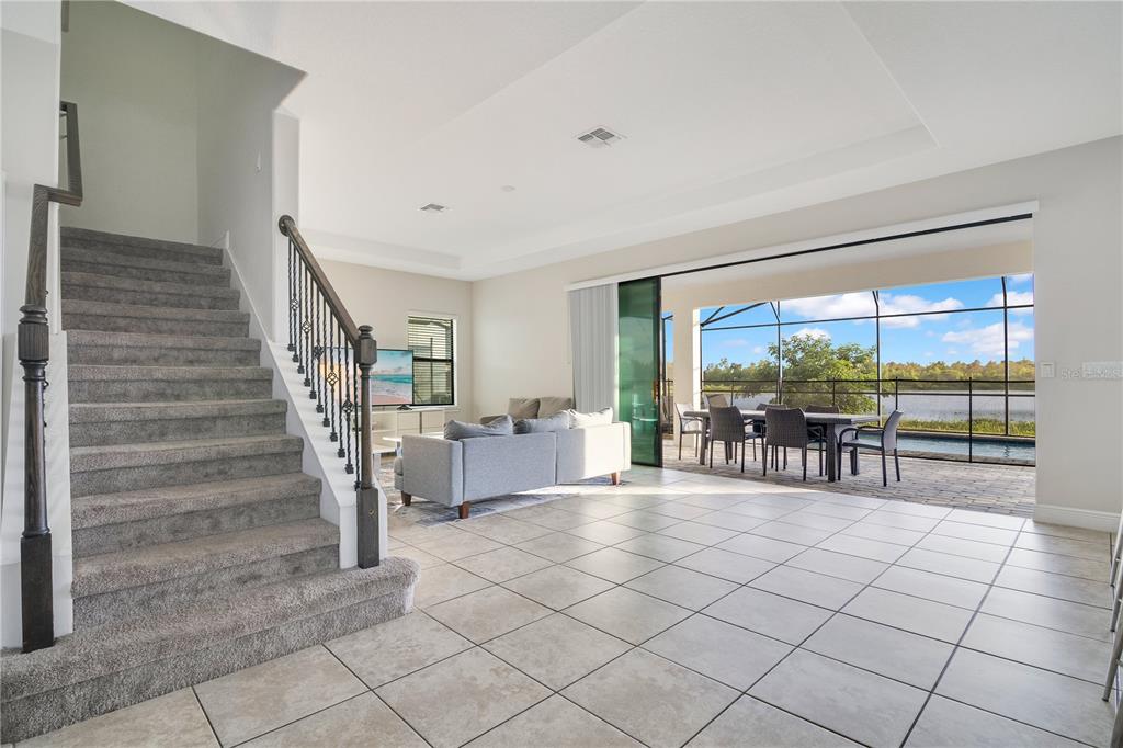 A living room with carpeted stairs, tile flooring, and a sliding door opening to a patio — 183 MITCHELLS MANOR, HAINES CITY, FL