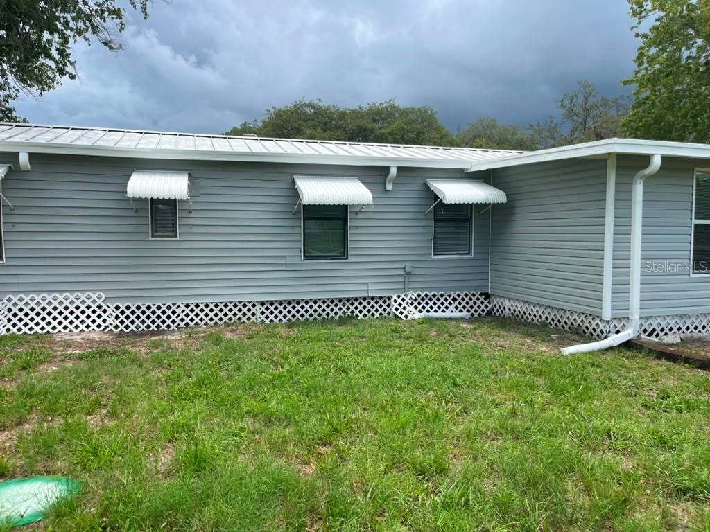 The exterior of a light gray mobile home features white lattice skirting and metal awnings — 14810 THOMPSON AVENUE, HUDSON, FL