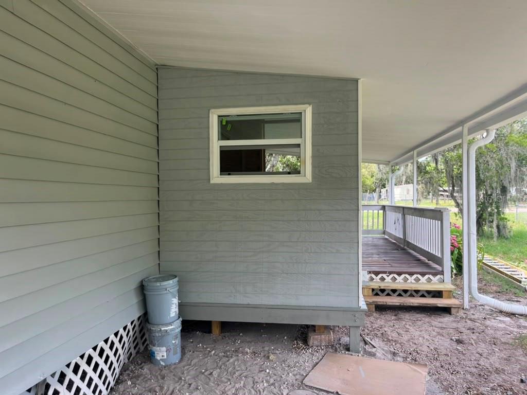 A view of a house exterior featuring gray siding, a window, and a wooden porch — 14810 THOMPSON AVENUE, HUDSON, FL