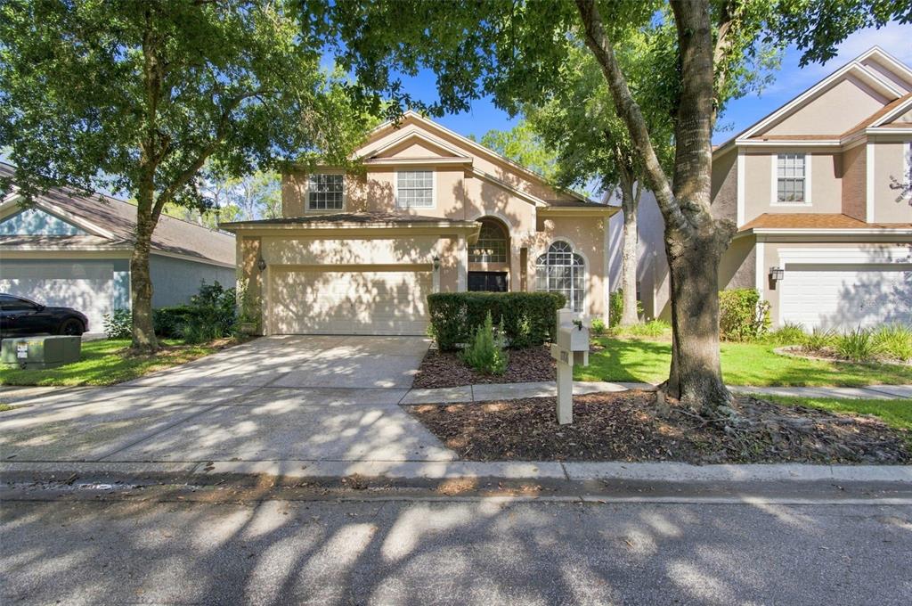 A two-story suburban house with a beige stucco exterior, a two-car garage, and mature trees — 17708 LONG RIDGE ROAD, TAMPA, FL