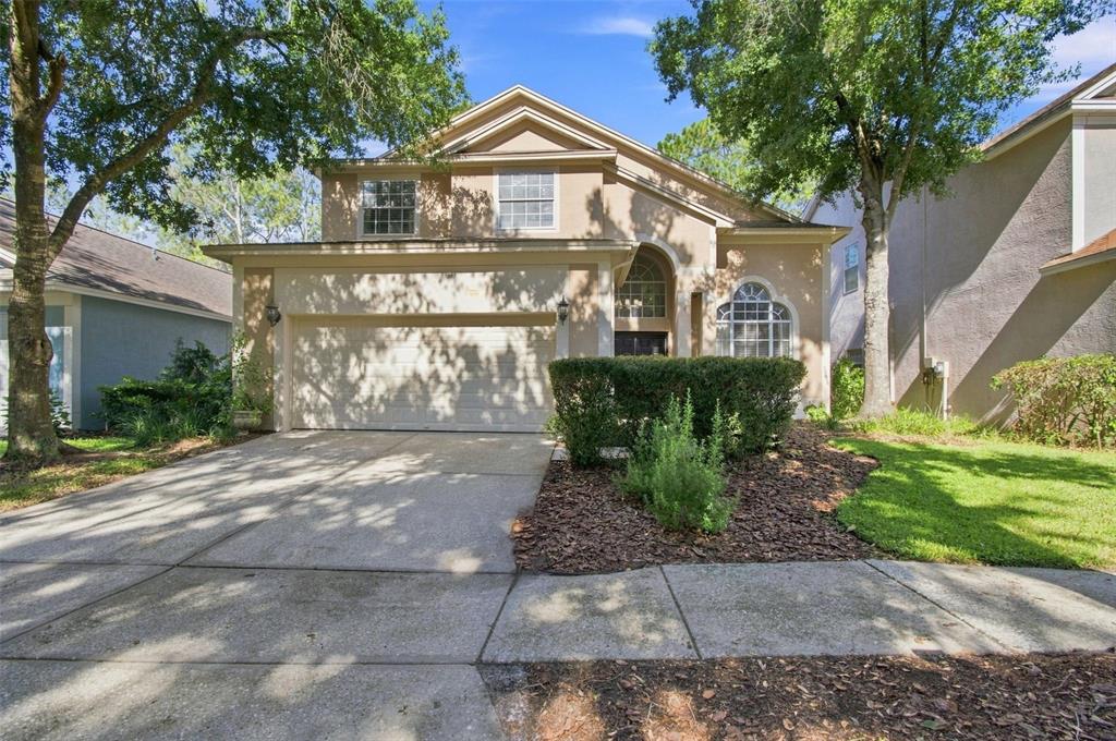 A two-story suburban house with a beige stucco exterior, a two-car garage, and mature trees — 17708 LONG RIDGE ROAD, TAMPA, FL
