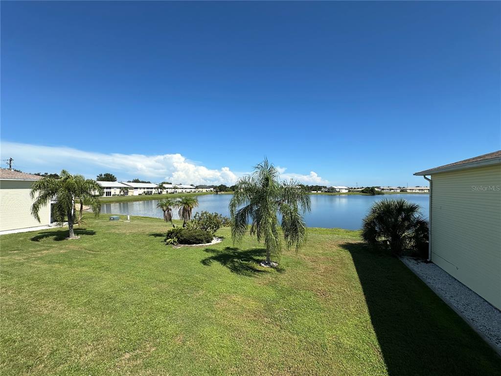 A grassy backyard with palm trees overlooks a lake behind two residential buildings — 26282 RAMPART BOULEVARD UNIT 207G, PUNTA GORDA, FL