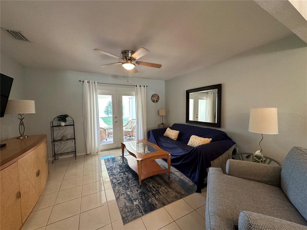 A living room features tile floors, a ceiling fan, a sofa with a cover, and patio doors — 26282 RAMPART BOULEVARD UNIT 207G, PUNTA GORDA, FL