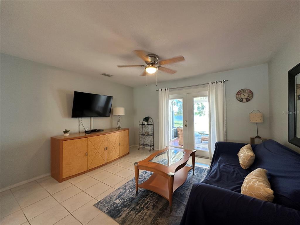 A living room features tile flooring, a blue sofa, a wooden media console, and glass doors — 26282 RAMPART BOULEVARD UNIT 207G, PUNTA GORDA, FL