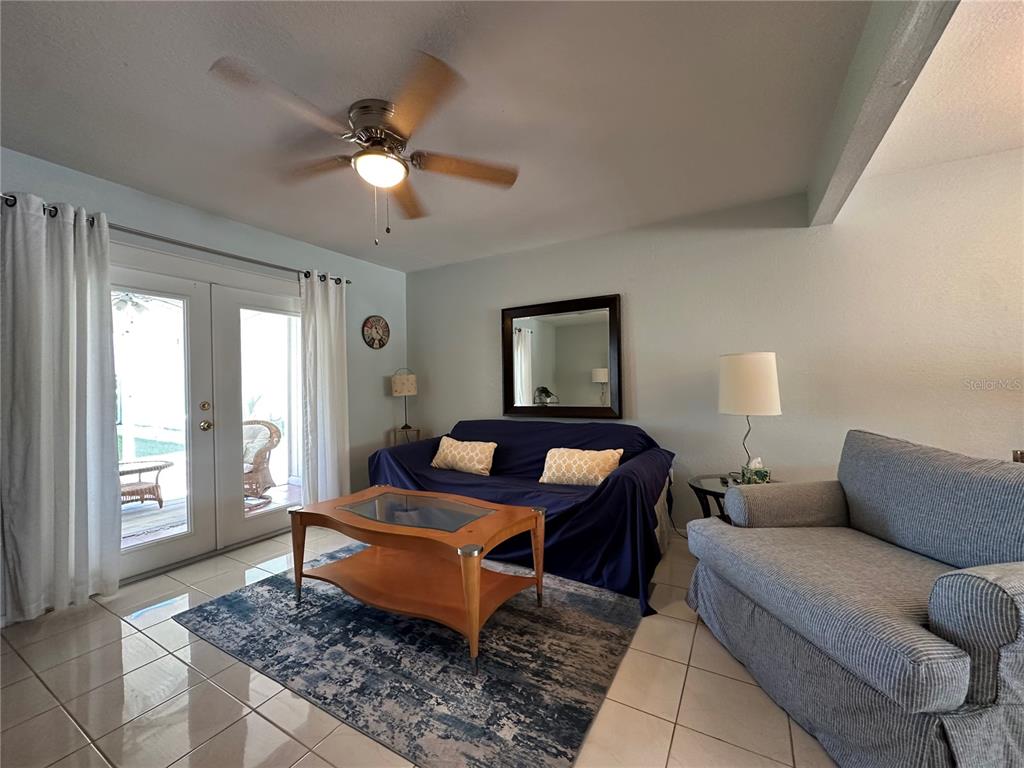 A living room features tile floors, a ceiling fan, a blue sofa, and glass doors — 26282 RAMPART BOULEVARD UNIT 207G, PUNTA GORDA, FL