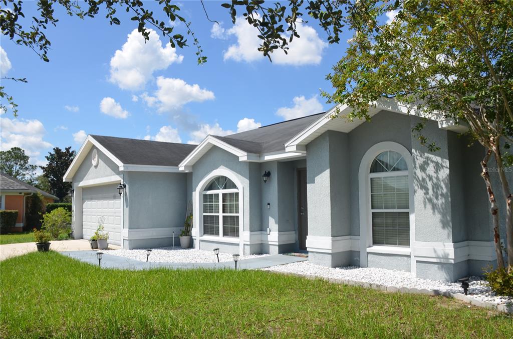 A single-story gray house with a two-car garage, white trim, and a white rock garden — 9916 SW 56TH AVENUE, OCALA, FL