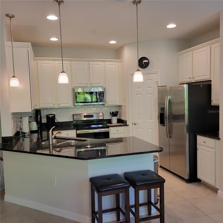 A kitchen features white cabinets, dark granite countertops, stainless steel appliances, and a breakfast bar — 152 NAVIGATION CIRCLE UNIT 107, OSPREY, FL
