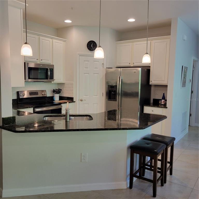 A kitchen with white cabinets, dark granite countertops, stainless steel appliances, and a breakfast bar — 152 NAVIGATION CIRCLE UNIT 107, OSPREY, FL