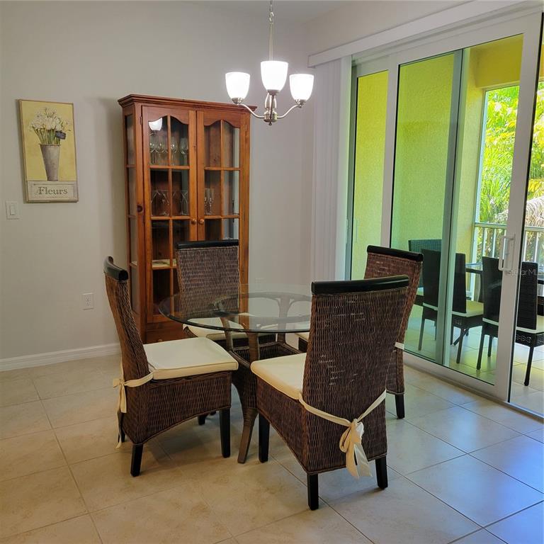 A dining room features a glass-topped table, wicker chairs, a wooden hutch, and sliding glass doors — 152 NAVIGATION CIRCLE UNIT 107, OSPREY, FL