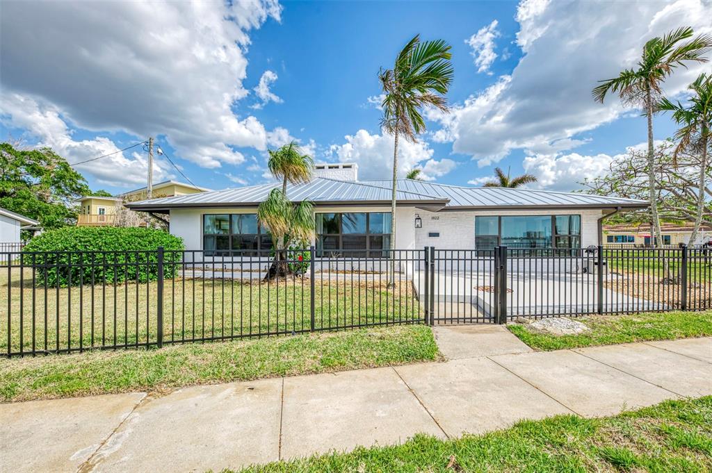 A single-story white house with a metal roof sits behind a black metal fence — 1822 RIVERSIDE DRIVE E, BRADENTON, FL