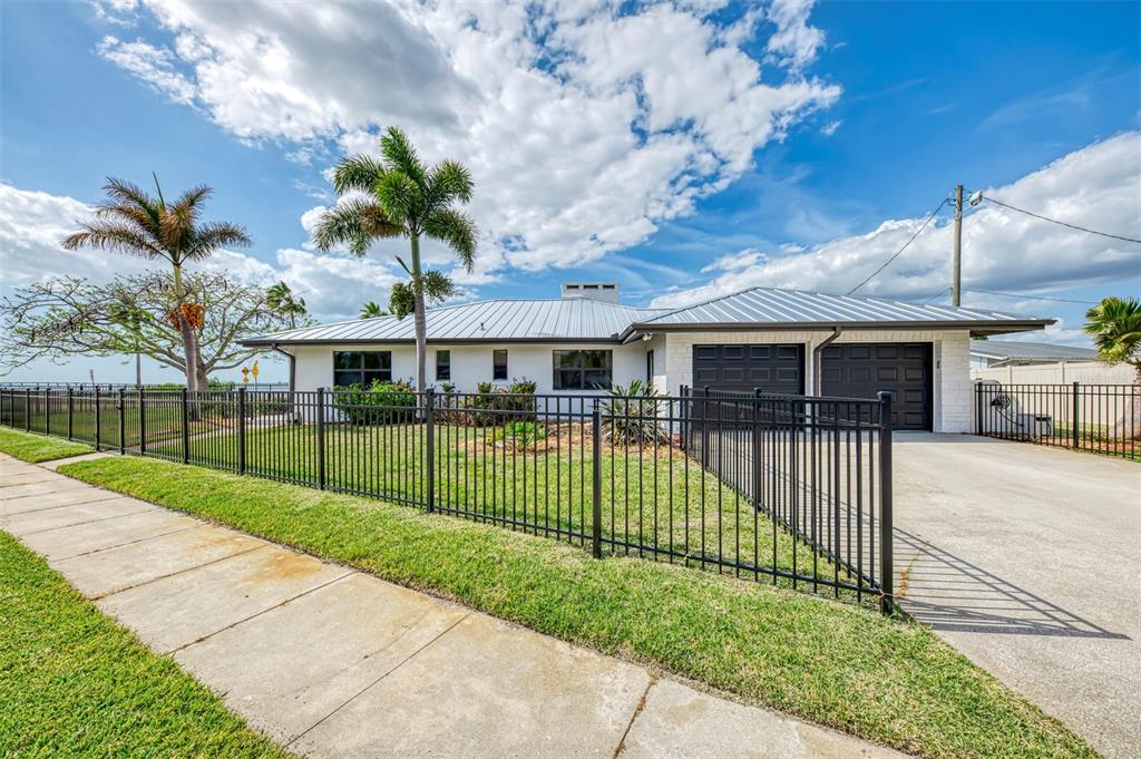 A single-story house with a metal roof, black garage doors, and a black metal fence — 1822 RIVERSIDE DRIVE E, BRADENTON, FL