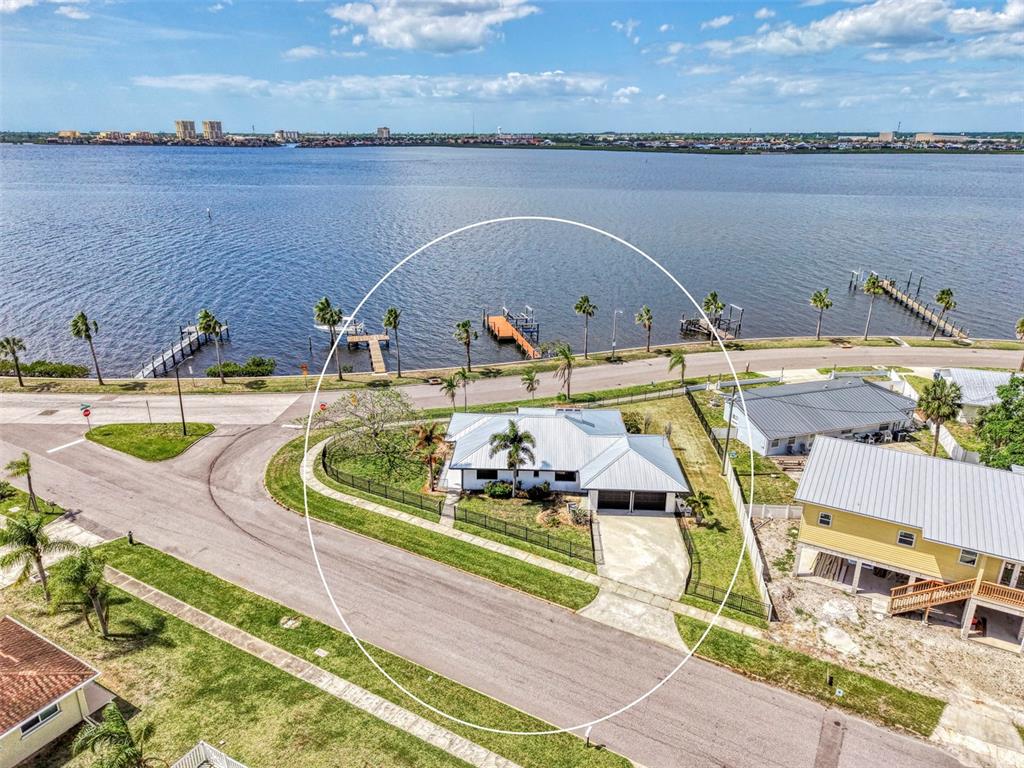 An aerial view shows a single-story house with a metal roof near a waterfront road — 1822 RIVERSIDE DRIVE E, BRADENTON, FL