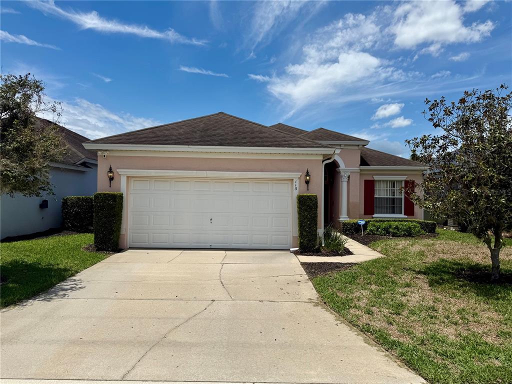 A single-story house with a beige stucco exterior, a two-car garage, and red window shutters — 113 PLUMOSO LOOP, DAVENPORT, FL