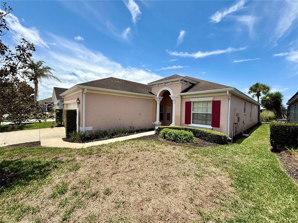 A single-story pink house with a arched entryway and red shutters under a blue sky — 113 PLUMOSO LOOP, DAVENPORT, FL