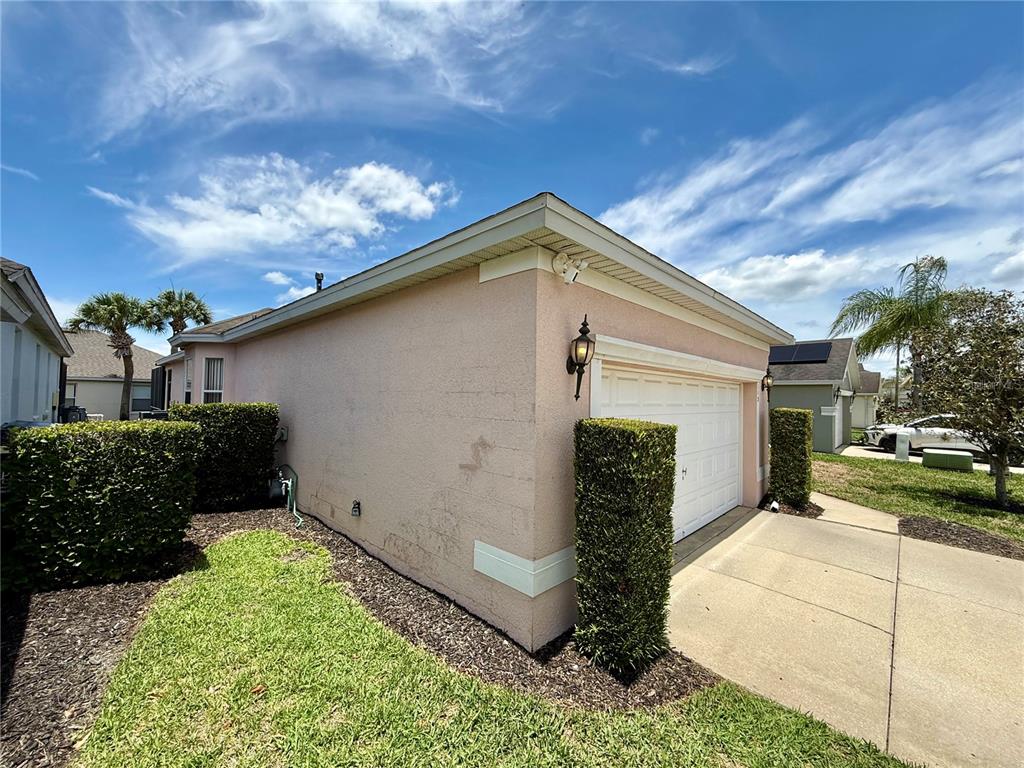 A side view of a peach-colored house with a garage and manicured hedges — 113 PLUMOSO LOOP, DAVENPORT, FL