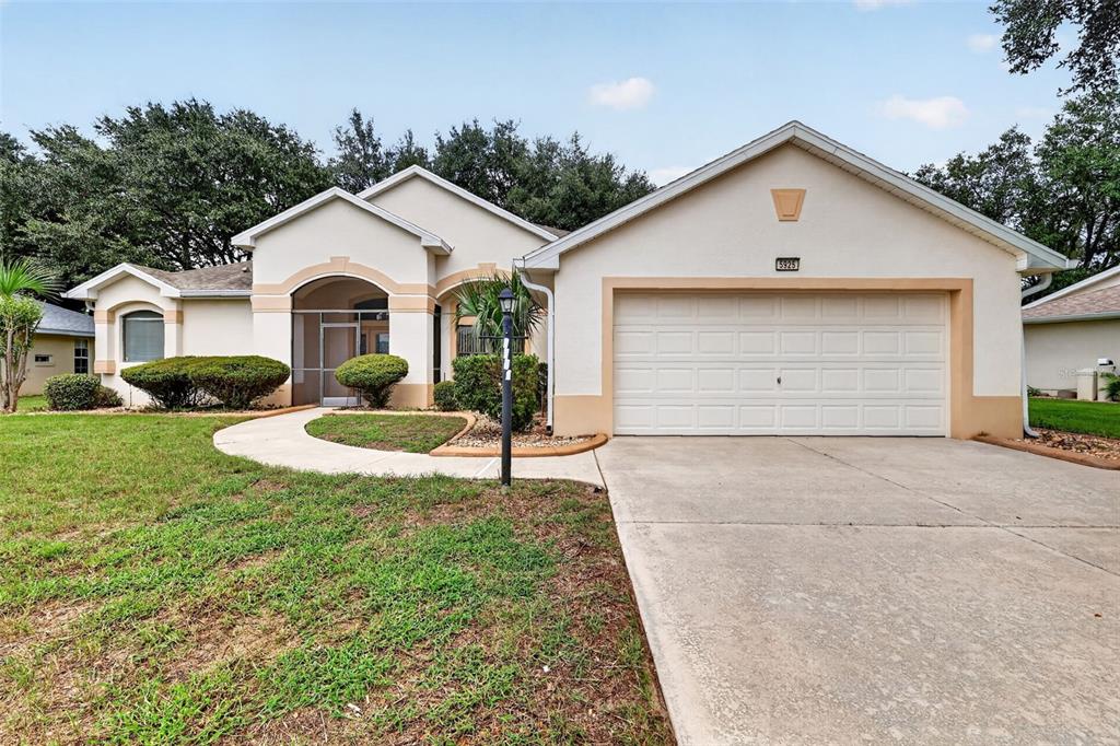 A single-story house with a beige stucco exterior, a two-car garage, and a front walkway — 5925 BAG PIPE PLACE, LEESBURG, FL