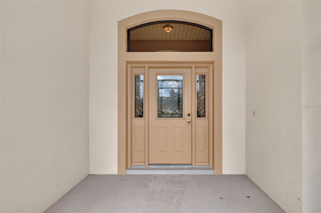 A tan front door with glass panels and a transom window sits under a covered porch — 5925 BAG PIPE PLACE, LEESBURG, FL