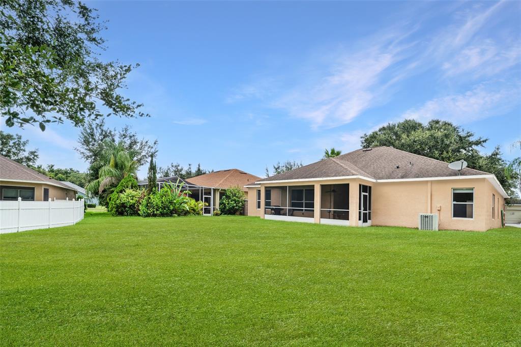 A backyard with a green lawn, a tan house with a screened porch, and fencing — 10903 WILDCAT DRIVE, RIVERVIEW, FL