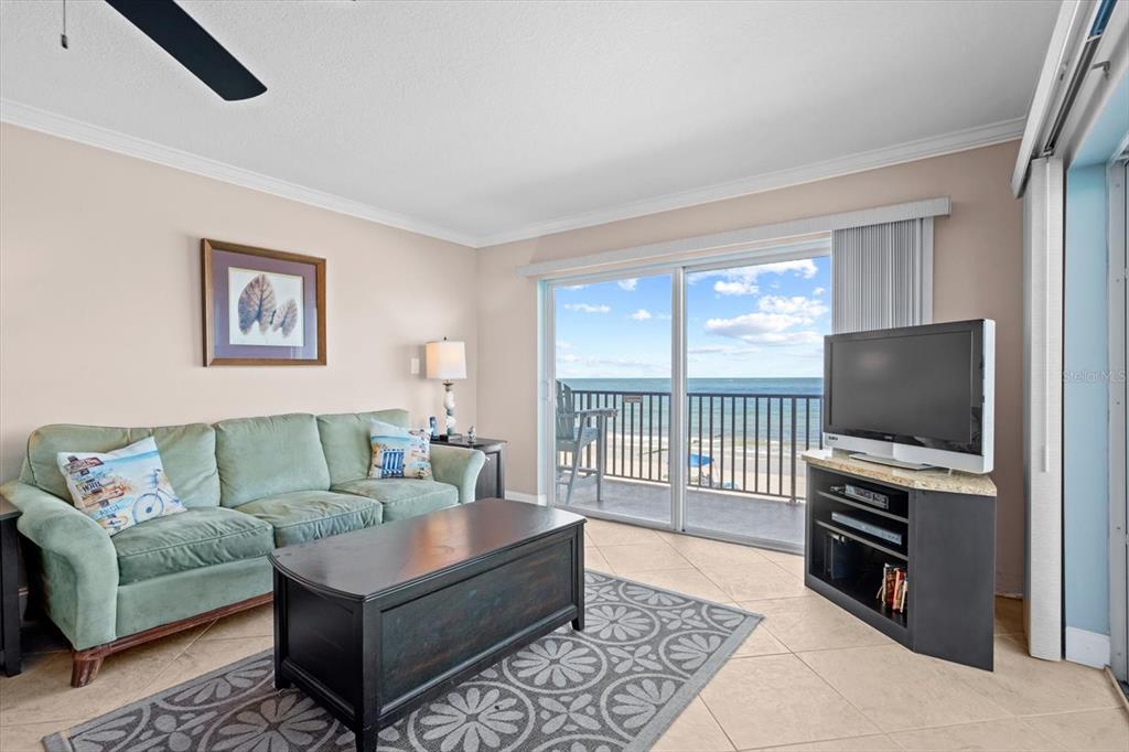 A living room features a green sofa, dark coffee table, television, and a balcony overlooking ocean — 14300 GULF BOULEVARD UNIT 206, MADEIRA BEACH, FL