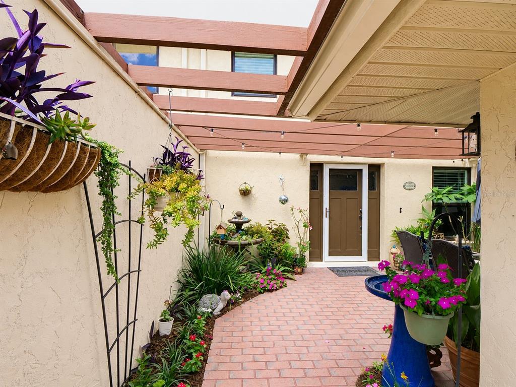 A brick patio features a blue birdbath, hanging planters, and a wooden pergola overhead — 100 S TREMAIN STREET UNIT G2, MOUNT DORA, FL