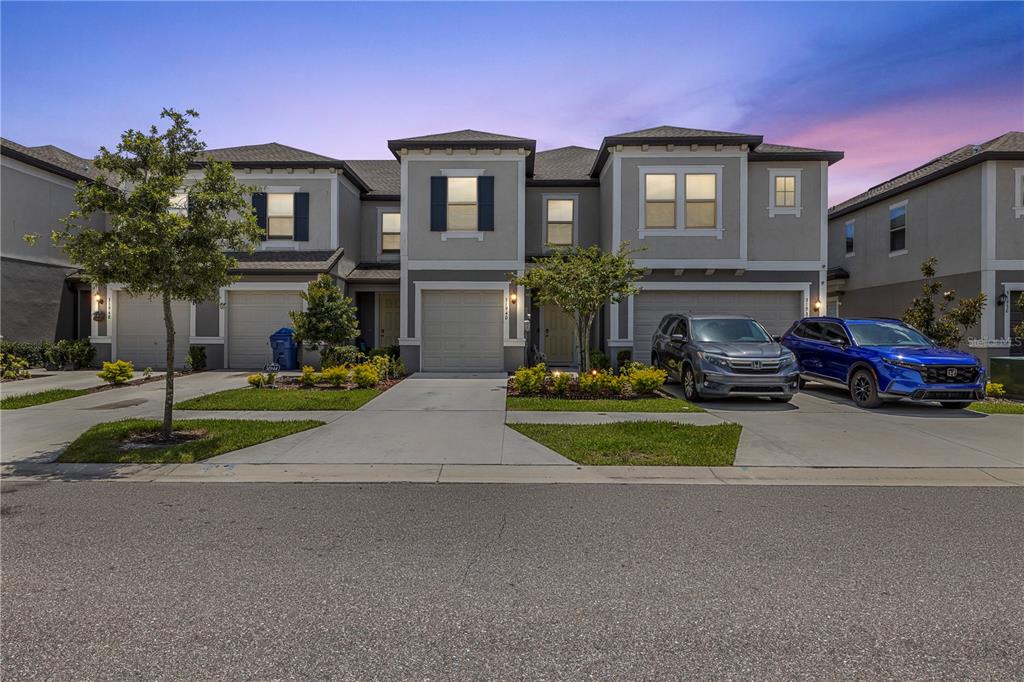 A row of three two-story townhouses with attached garages and concrete driveways at dusk — 31940 BLUE PASSING LOOP, WESLEY CHAPEL, FL