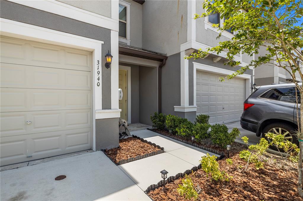 The exterior of a two-story townhouse features two garage doors, a recessed entryway, and landscaping — 31940 BLUE PASSING LOOP, WESLEY CHAPEL, FL