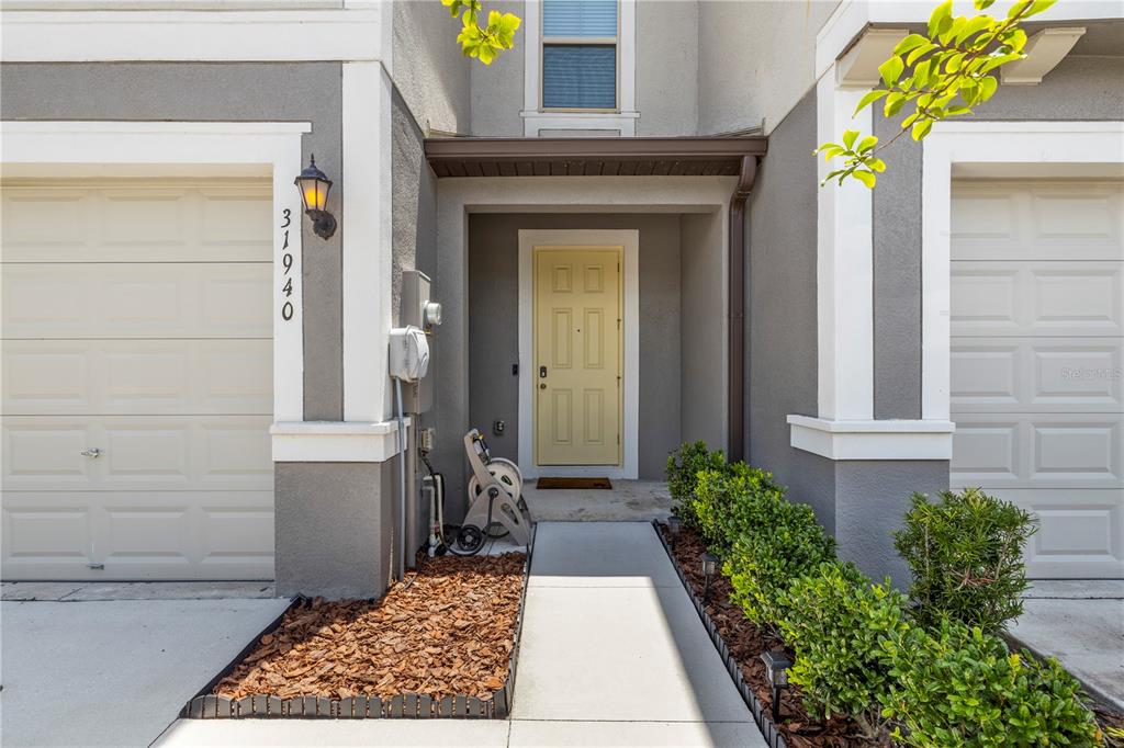 The exterior of a two-story townhouse features a yellow front door and two garage doors — 31940 BLUE PASSING LOOP, WESLEY CHAPEL, FL
