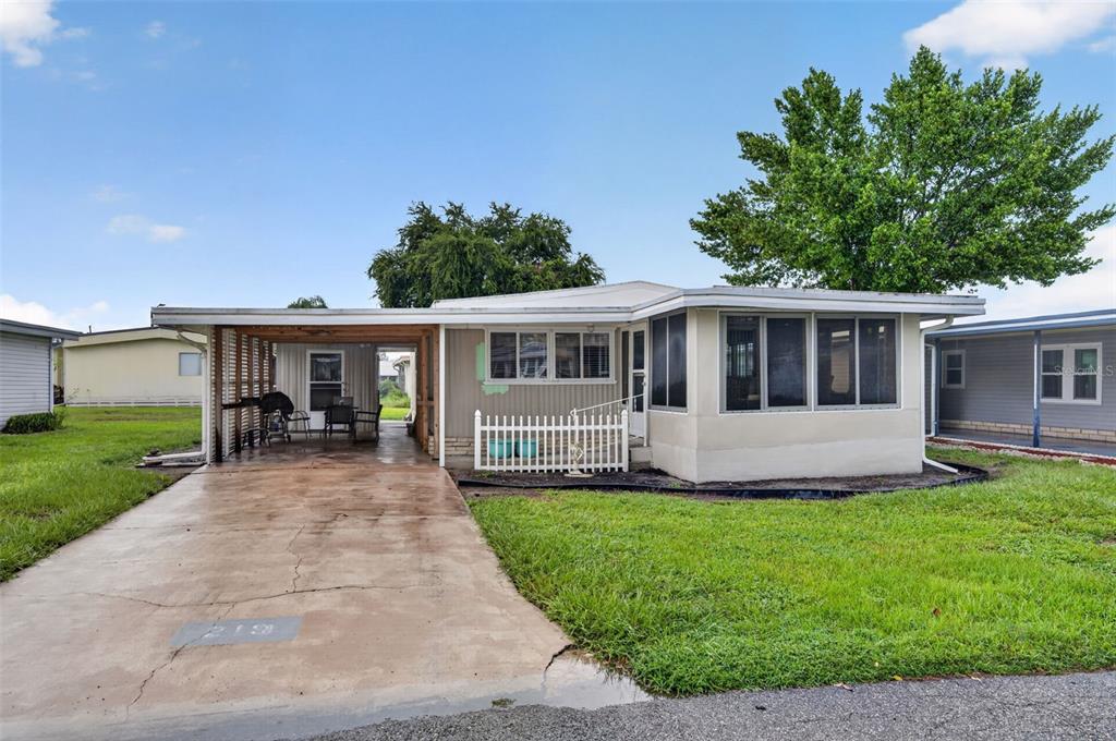 A single-story manufactured home with a carport, a white picket fence, and a screened-in porch — 219 PARADISE S, LEESBURG, FL
