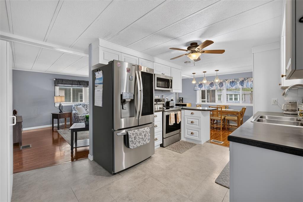 A kitchen with stainless steel appliances, white cabinets, and a tile floor, opening to a dining area — 219 PARADISE S, LEESBURG, FL