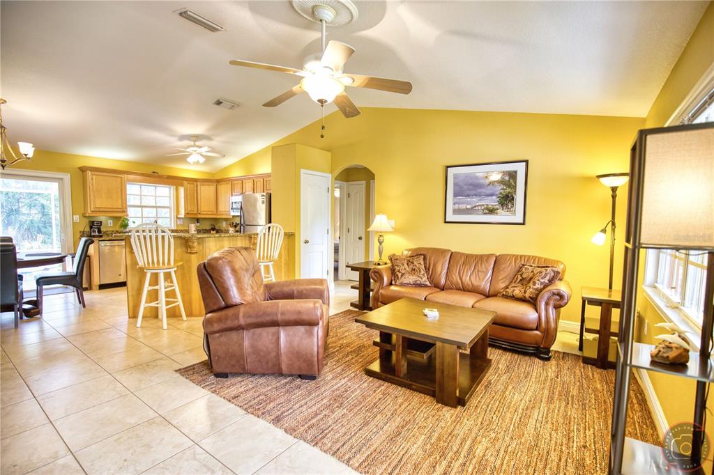 A living room with yellow walls, tile flooring, a leather sofa, and an open kitchen — 3471 DATURA ROAD, VENICE, FL