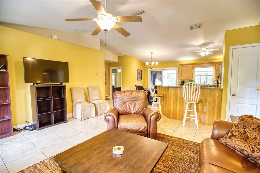 A living room with yellow walls, tile flooring, a leather armchair, and an open kitchen — 3471 DATURA ROAD, VENICE, FL