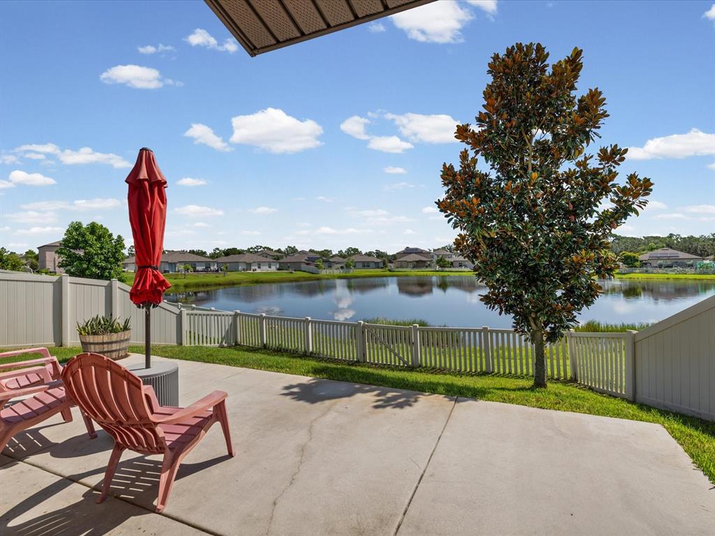 A concrete patio overlooks a pond with a red umbrella and a large magnolia tree — 15416 WICKED STRONG STREET, RUSKIN, FL