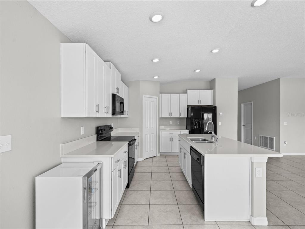 A kitchen features white cabinetry, a central island, black appliances, and light-colored tile flooring — 15416 WICKED STRONG STREET, RUSKIN, FL
