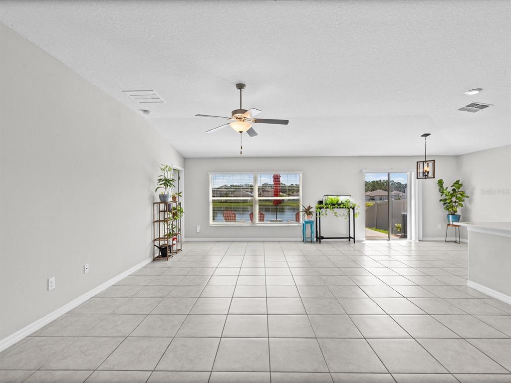 A spacious, tiled living area features a ceiling fan, large windows, and a sliding glass door — 15416 WICKED STRONG STREET, RUSKIN, FL