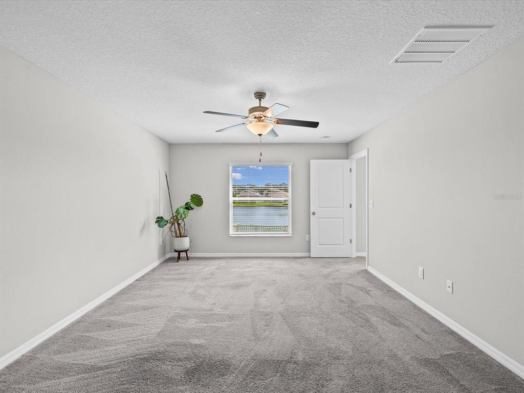 A carpeted bedroom features a ceiling fan, a window overlooking a lake, and a white door — 15416 WICKED STRONG STREET, RUSKIN, FL